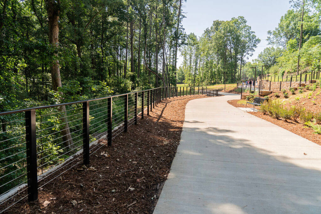 Alpha Loop path in sunny June 2024. A wide multi-modal cement trail curves along new modern fencing and tall trees.